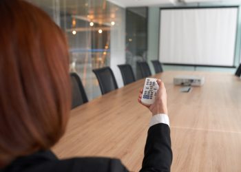 Using projector in meeting room Business woman using remote control for projector